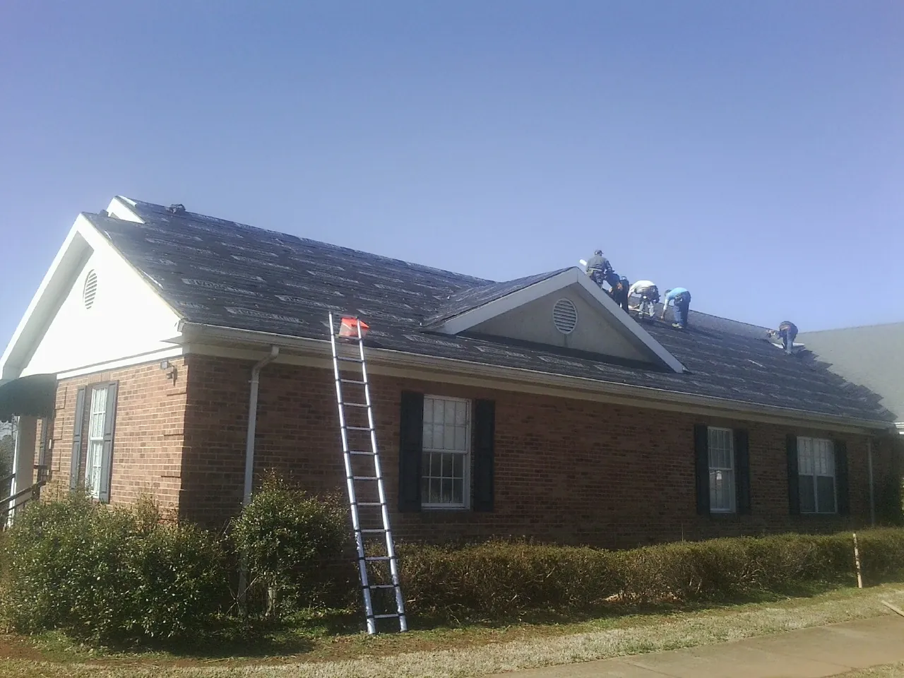 Crew tearing shingles off a brick ranch roof with a ladder set — Metal Roof Repair work by our crew in Mill Creek